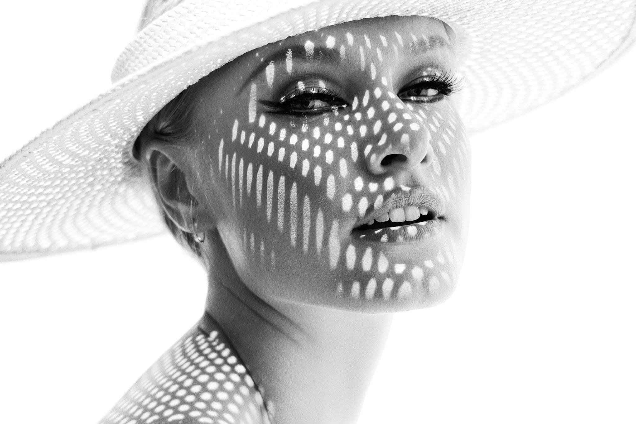 Woman in white brimmed hat with holes that's casting high contrast shadows on her face.